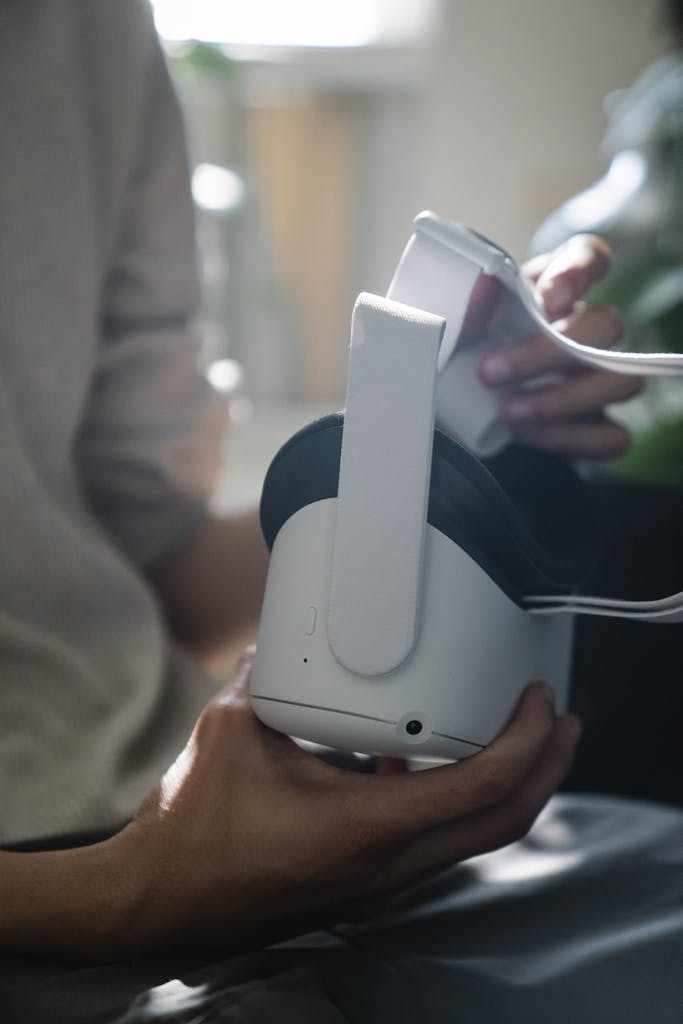 Crop unrecognizable male teenager in casual clothes holding modern headset of virtual reality at home in sunlight