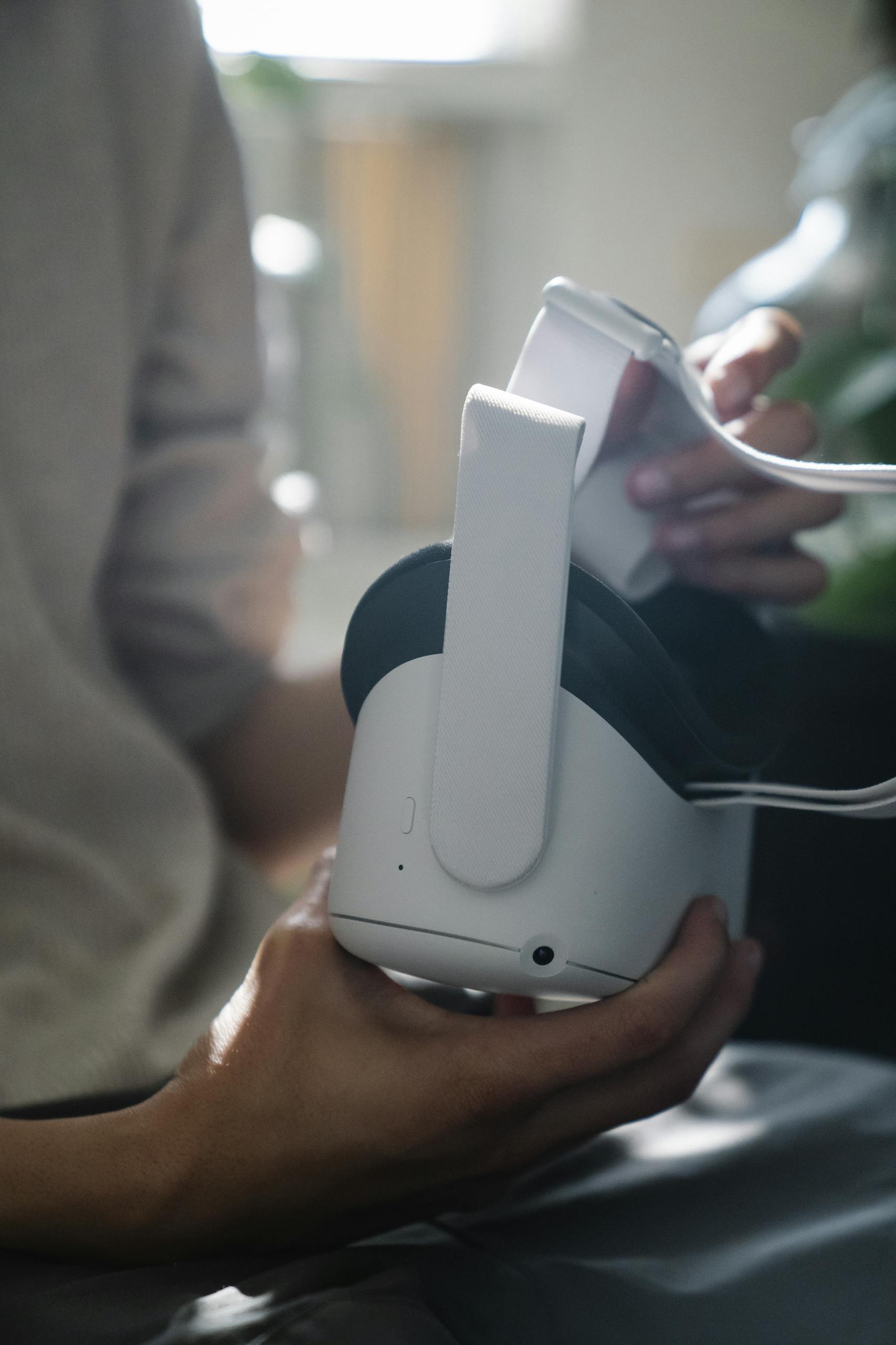 Crop unrecognizable male teenager in casual clothes holding modern headset of virtual reality at home in sunlight