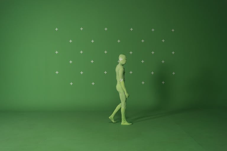 Person walking in a chroma key suit in a studio with green screen for video editing.