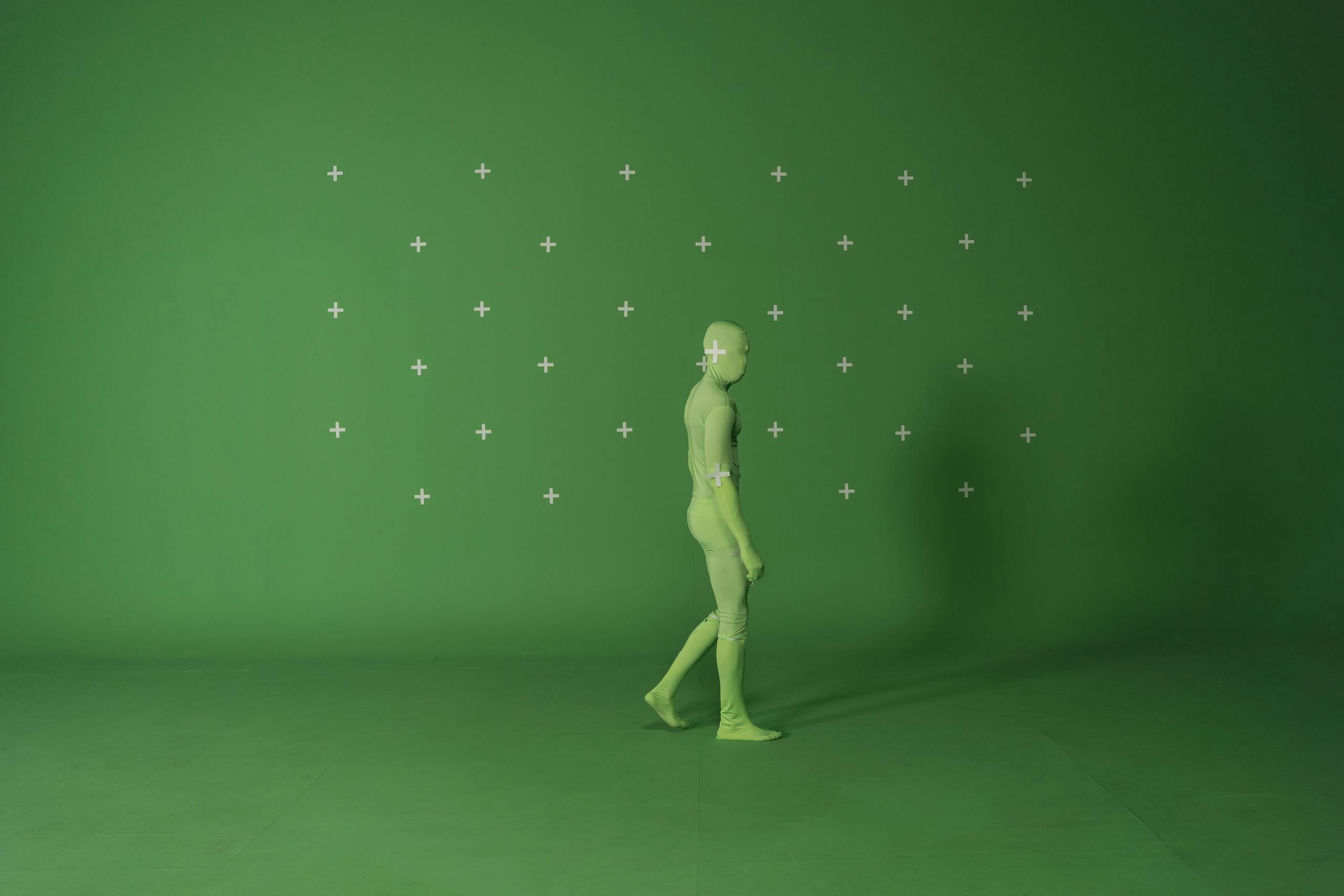 Person walking in a chroma key suit in a studio with green screen for video editing.